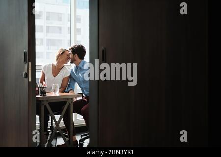 Two Co-Workers Sitting At Office Desk And Kissing Stock Photo