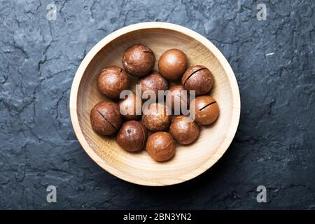 Dried organic Macadamia nuts in wooden bowl closeup. Studio macro shoot. Black concrete background Stock Photo