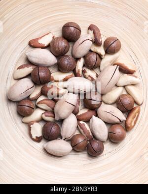 Dried mixed nuts in wooden bowl closeup. Macadamia, Pecan and Brazil nuts with knife on wooden table. Studio macro shoot. Stock Photo