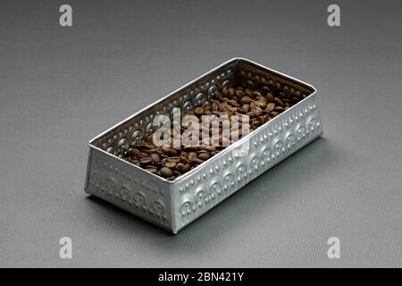 Roasted coffee beans are placed in aluminum box containers on a gray base. Stock Photo
