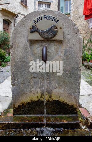 An old fountain, labeled 'EAU POTABLE' (potable water), with an image of a fish, distributes water in the town of Saint-Paul-de-Vence, France Stock Photo