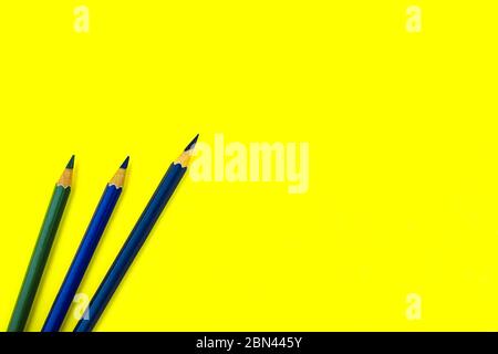 Three dark blue colored wood pencil crayon placed on top of a yellow paper background Stock Photo