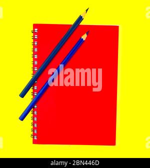 Two blue color wood pencil crayons placed on top of a deep red color note paper diary Stock Photo