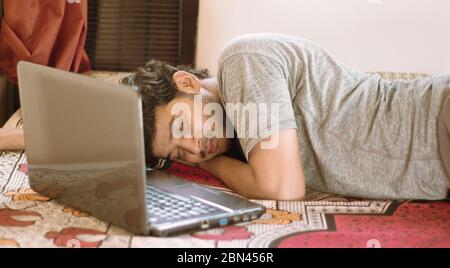Tired young man sleeping in bed with laptop - hard work, laziness of working from home or WFH during coronavirus or covid-19 lock down concept. Stock Photo