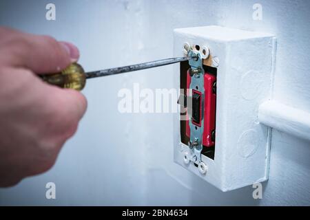 Man's hand using screwdriver to replace/repair 20 amp lightswitch on wall. Stock Photo