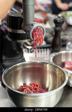 Meat grinder in action and ground beef meat. electric meat grinder.  Unidentifiable butcher holding tray full of minced raw red meat leaving  machine in Stock Photo - Alamy