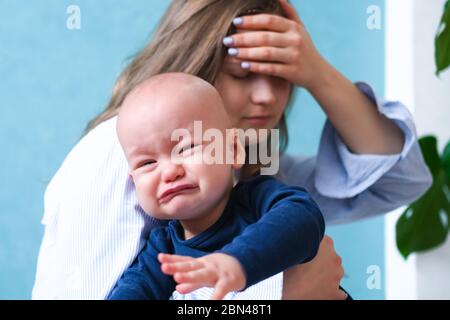 Mom tired trying to calm her crying baby. Newborn tantrum child on mother hands. Family life, motherhood Stock Photo