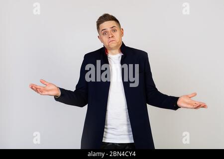Attractive young man male shrugs with a lost expression. The guy makes an ignorant gesture, not having the slightest idea. I doubt the concept. Stock Photo