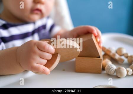 eco wood toys. baby game. Little clever caucasian child playing natural toys on highchair. games for early development. Toy in kids hands close up. Stock Photo