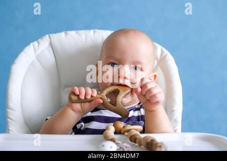eco wood toys. baby game. Little clever caucasian child playing natural toys on highchair. games for early development. Toy in kids mouth. Stock Photo