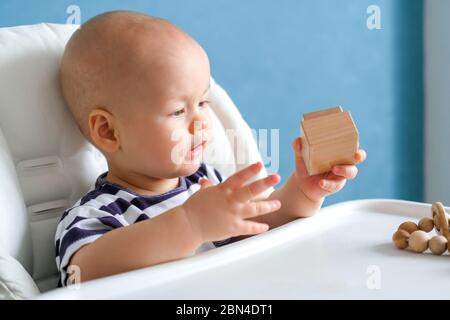 eco wood toys. baby game. Little clever caucasian child playing natural toys on highchair. games for early development. Toy in kids hands close up. Stock Photo