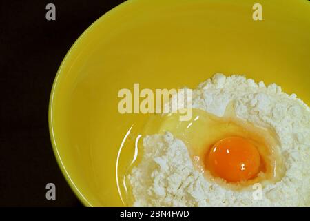 Closeup cracked egg on raw flour in a yellow mixing bowl Stock Photo
