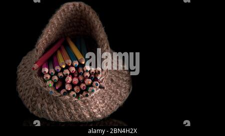 colored pencils in a knitted basket on a black background Stock Photo
