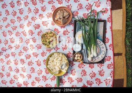 Top view of a picnic setting - cauliflower salad, couscous risotto, home made sourdough bread and fresh scallions placed on a blanket outside on  gras