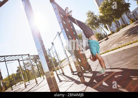 Staying in great shape. Strong and healthy mature or middle aged man in sportswear doing handstand while training outdoors in the morning Stock Photo
