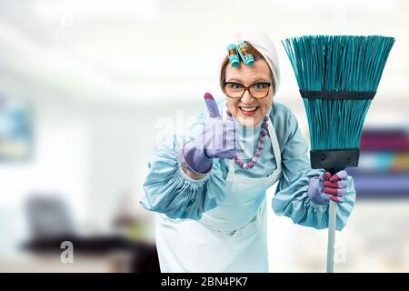 Portrait of a cleaning lady with a cleaning broom in hands. A cleaning lady in uniform is standing against a bright office. Stock Photo