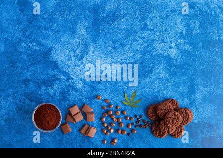 Cannabis cookies, cocoa, hemp seeds and coffee beans on dark blue background. Medicinal marijuana in food. Stock Photo