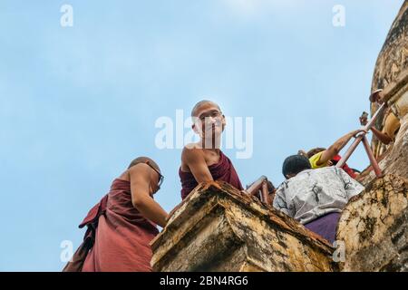 Bagan Myanmar - October 29 2013; Monk climbing steps up a stupa looks over edge and smiles calmly.