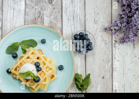 Fresh baked homemade classic Belgian waffles topped with icecream, fresh blueberries and mint on wooden background, top down view. Savory waffles Stock Photo