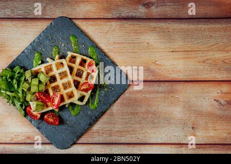 Fresh baked Belgian waffles with arugula, tomatoes and avocado on black a plate. Savory waffles. Breakfast concept. Healthy breakfast Stock Photo