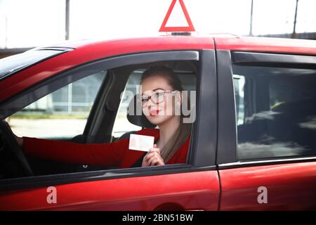 Joyful girl driving a training car with a drivers license card in her hands Stock Photo