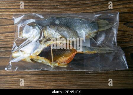 Dried salted crucian fishes in a transparent package on wooden background. Snack to beer Stock Photo