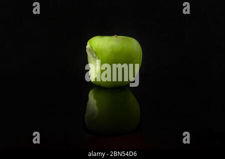 Bitten green apple with reflection on black background. Stock Photo