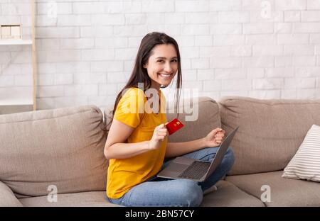 Home shopping. Pretty girl with credit card and laptop buying goods online, indoors Stock Photo