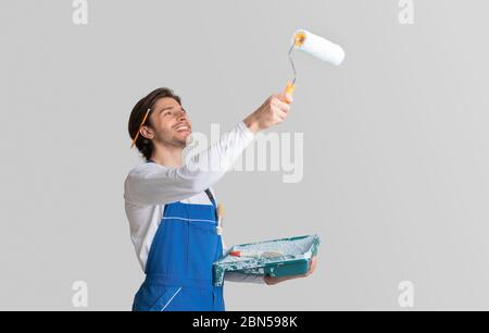 Happy painter dressed in work clothes painting ceiling with roller Stock Photo