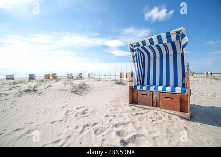 Blue and white striped wooden beach chair or bench on a white sandy tropical empty beach during a hot summer day. vacation travel destination or aband Stock Photo