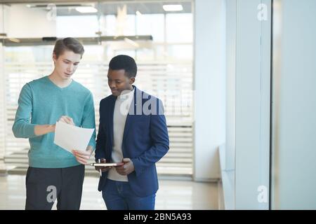 Waist up portrait of two young businessmen discussing work documents while standing in while office interior, copy space Stock Photo