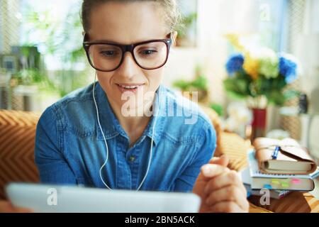 happy stylish housewife in jeans shirt with white headphones and tablet PC study online in the modern living room in sunny day. Stock Photo
