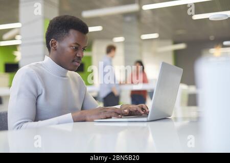 Side view portrait of smiling young African man using laptop at work, copy space Stock Photo