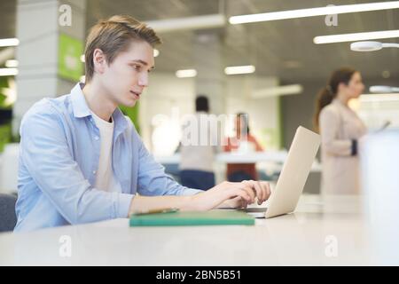 Side view portrait of young man using laptop at work in office, copy space Stock Photo