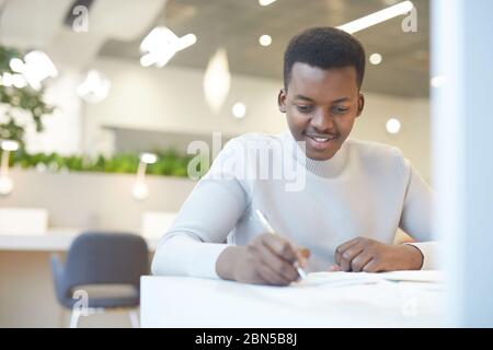 Portrait of smiling young African man using laptop at work, copy space Stock Photo
