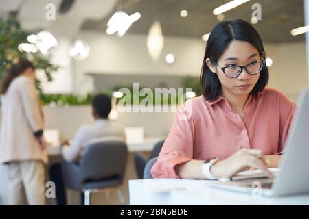 Portrait of young Asian woman using laptop while studying in cafe, copy space