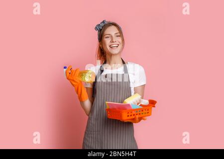 Excited young housewife wearing apron posing with cleaning tools in hands Stock Photo