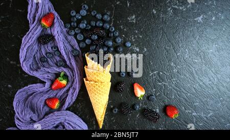Summer berries creative flatlay top view with blueberries and blackberries in ice cream waffle cone. Dark moody creative composition with negative cop Stock Photo