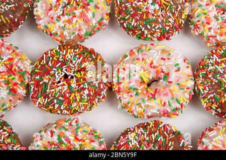 Close up on  cake donuts with sprinkles, chocolate and vanilla frosting covered in rainbow sprinkles. A popular American junk food. Stock Photo