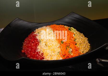 Large portion of vegetable salad on a black bowl. Chopped tomatoes, corn, cheese, lettuce and carrot. Stock Photo