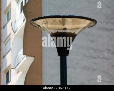 modern street light of circular design and clear glass lens on top of aluminum light pole. blurred apartment building concrete exterior and balconies Stock Photo