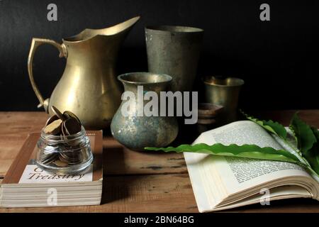 Old vintage utensils with book and Indian rupee coins. Old brass metal utensils on wooden table floor. Stock Photo