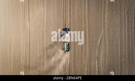 Aerial view of a blue tractor working in a field with a fertilizer and seed spreader Stock Photo