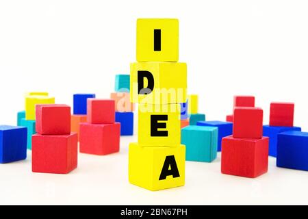 Word IDEA stacked of yellow wooden cubes and a lot of multicoloured toy blocks in the background. Idea building concept. Stock Photo