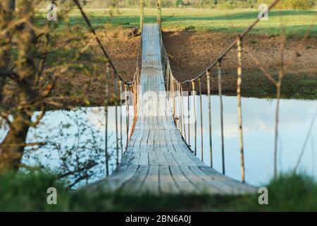 Old suspended wooden foot bridge over the river. Photo on a summer day. River crossing for people