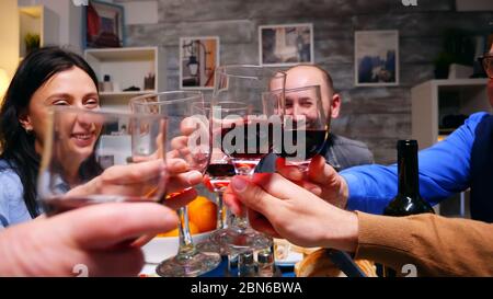 Zoom in shot of family clinking glasses of red wine at dinner over the table. Stock Photo