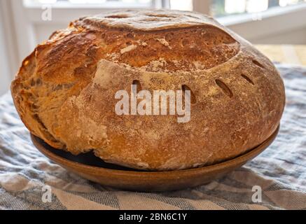 Freshly made Sourdough bread. The freshly made sourdough loaf sits a cloth covered table in a rustic kitchen. The bread has a golden crusty outside. Stock Photo