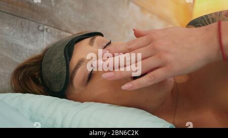 Closeup beautiful woman in pajamas yawning while covering eyes with sleep mask. Stock Photo