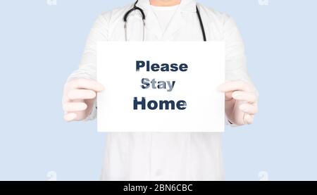 Doctor showing paper with text please stay home, Isolated over blue background. Stock Photo