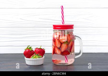 Strawberry infused water, cocktail, lemonade or tea. Summer iced cold drink with strawberry, lemon and leaf of mint on white wooden background. Flat Stock Photo